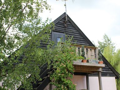 An exterior view of a building with a wooden balcony and stairs surrounded by green trees at The Hayloft in Necton near Swaffham