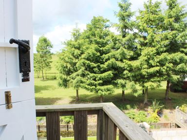 A view of green trees and grassy land from a wooden balcony with a partially open white door at The Hayloft in Necton near Swaffham