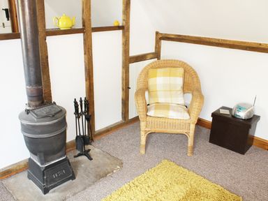 A corner of a room with a wood stove a wicker chair with cushions and a small table with a radio at The Hayloft in Necton near Swaffham