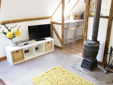 A living room with a television on a white stand a vase with flowers a wood stove and stools at The Hayloft in Necton near Swaffham
