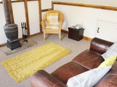 A living room with a wood-burning stove wicker chair yellow rug and leather sofa at The Hayloft Necton near Swaffham