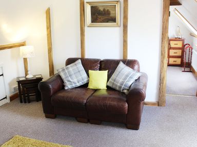 A brown leather sofa with three cushions and a lamp on a side table in a living room at The Hayloft in Necton near Swaffham