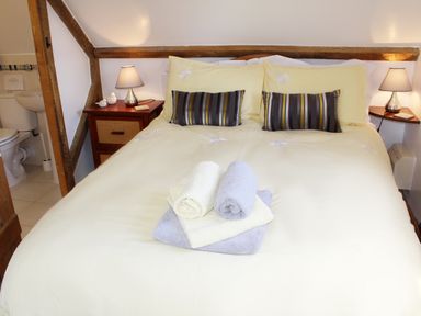 A bedroom with a double bed pillows bedside tables lamps and a view into a bathroom at The Hayloft in Necton near Swaffham
