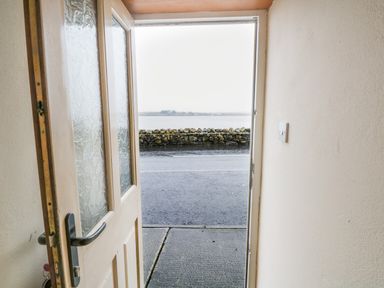 An open door showing a view of a road a stone wall and water beyond at Quayside House in Roundstone County Galway