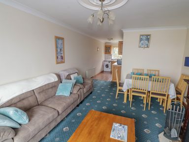 A living room with a beige sofa and blue cushions a wooden dining table with six chairs and a kitchen in the background at Quayside House in Roundstone County Galway