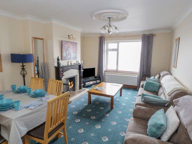 A living room with a dining table set with blue dishes a fireplace a flat screen tv and a sofa with pillows at Quayside House in Roundstone County Galway