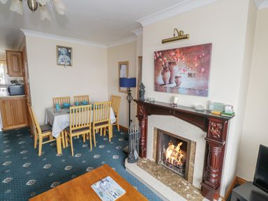 A dining area with wooden chairs and table set with blue dishes next to a lit fireplace with a framed painting above at Quayside House in Roundstone County Galway