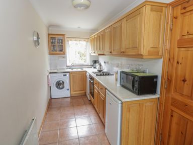A kitchen with wooden cabinets a washing machine a microwave a stove and a sink at Quayside House in Roundstone County Galway