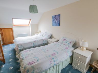 A bedroom with two beds bedside tables and a window at Quayside House in Roundstone County Galway