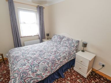 A bedroom with a double bed with patterned bedspread and two white bedside tables with lamps at Quayside House in Roundstone County Galway