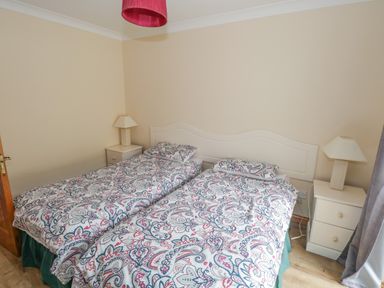 A bedroom with two single beds with patterned bedding two bedside tables with lamps and a wooden door at Quayside House in Roundstone County Galway