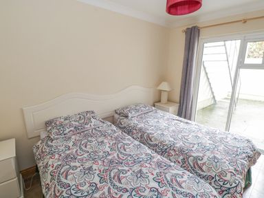 A bedroom with two single beds with patterned bedding a bedside table with a lamp and a sliding glass door with curtains at Quayside House in Roundstone County Galway