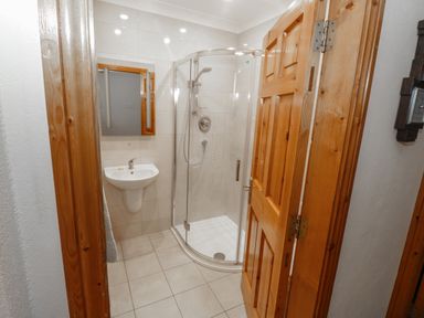 A bathroom with a corner shower cubicle and a wall-mounted sink at Quayside House in Roundstone County Galway