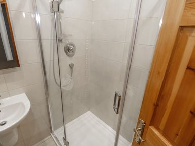 A bathroom with a glass enclosed shower and a white sink beside a wooden door at Quayside House in Roundstone County Galway