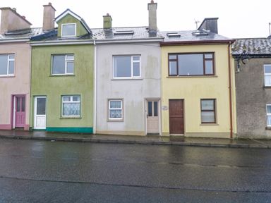 A row of terraced houses on a wet street with varying colors of green white and yellow at Quayside House in Roundstone County Galway
