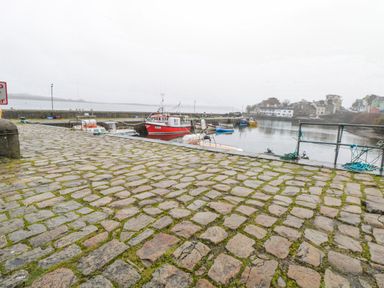 A stone-paved dock area with several boats moored in the water and buildings in the background at Quayside House in Roundstone County Galway