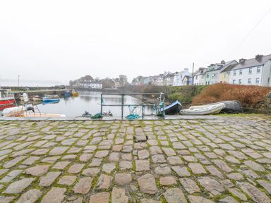 A harbor with boats moored along the water and a cobblestone path in front with houses in the background at Quayside House in Roundstone County Galway