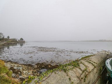 A coastal scene with rocks a stone wall and water at Quayside House in Roundstone County Galway