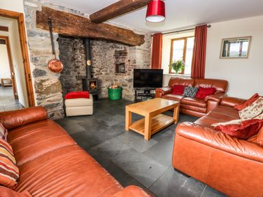 A living room with leather sofas a wooden coffee table a stone fireplace with a wood burner a television and red curtains at Maestyddyn Farm House Clawddnewydd near Ruthin