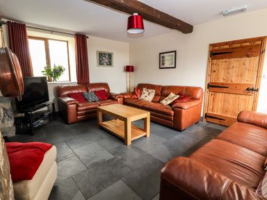 A living room with leather sofas a wooden coffee table a television and a wooden door at Maestyddyn Farm House in Clawddnewydd near Ruthin