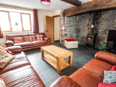 A living room with leather sofas a wooden coffee table a stone wall wood stove and a television at Maestyddyn Farm House Clawddnewydd near Ruthin