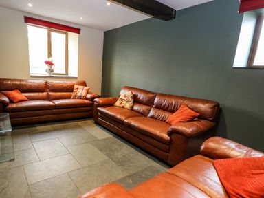 A sitting room with brown leather sofas and cushions and two windows at Maestyddyn Farm House Clawddnewydd near Ruthin