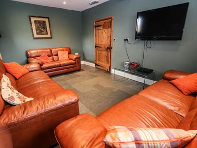 A living room with three brown leather sofas a wooden door a wall-mounted tv and a glass table at Maestyddyn Farm House in Clawddnewydd near Ruthin