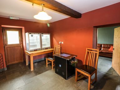 A room with stone floor tiles a wooden door orange painted walls two wooden chairs a table with two display refrigerators and a black arcade game machine at Maestyddyn Farm House Clawddnewydd near Ruthin