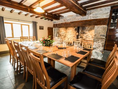 A dining room with a large wooden table set with glasses and placemats and wooden chairs with black cushions at Maestyddyn Farm House in Clawddnewydd near Ruthin