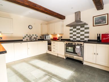 A kitchen with cream cabinets a stainless steel oven a tiled backsplash and wooden ceiling beams at Maestyddyn Farm House Clawddnewydd near Ruthin
