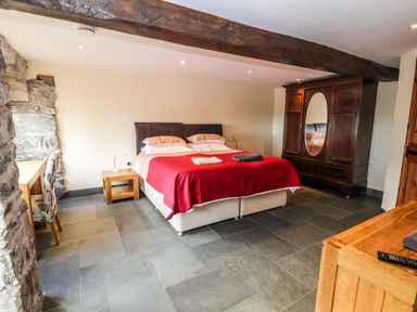 A bedroom with a double bed covered with a red blanket and wooden furniture including a wardrobe and a desk at Maestyddyn Farm House Clawddnewydd near Ruthin