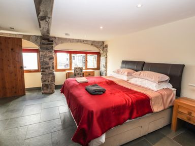 A bedroom with a bed covered in red bedding a wooden door stone window frames and a desk at Maestyddyn Farm House in Clawddnewydd near Ruthin