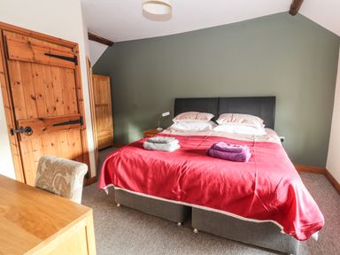 A bedroom with a double bed with red bedspread and folded towels on top at Maestyddyn Farm House in Clawddnewydd near Ruthin