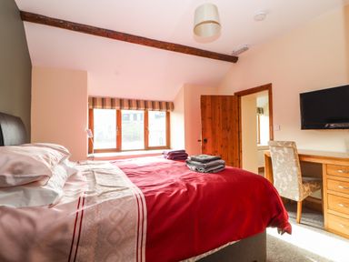 A bedroom with a red bedspread wooden desk and chair a wall-mounted television and a window at Maestyddyn Farm House in Clawddnewydd near Ruthin