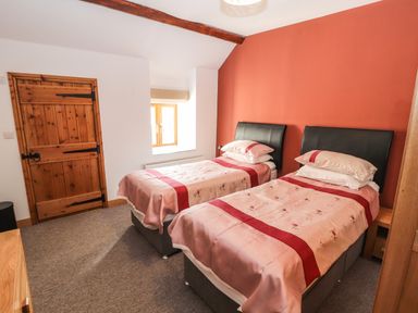 A bedroom with two single beds and a wooden door at Maestyddyn Farm House in Clawddnewydd near Ruthin