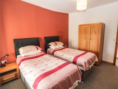 A bedroom with two single beds a wooden wardrobe a bedside table with a lamp and a red accent wall at Maestyddyn Farm House Clawddnewydd near Ruthin