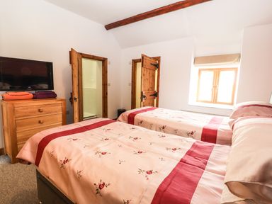 A bedroom with two beds covered with floral bedding a wooden dresser with a tv on top towels on the dresser two wooden doors and a window with blinds at Maestyddyn Farm House Clawddnewydd near Ruthin