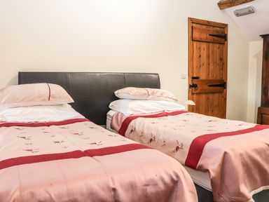 A bedroom with two single beds with pink and red bedding next to a wooden door at Maestyddyn Farm House in Clawddnewydd near Ruthin