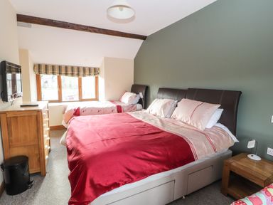 A bedroom with a double bed and a single bed under a window with a wooden chest of drawers and a bedside table at Maestyddyn Farm House in Clawddnewydd near Ruthin