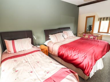 A bedroom with a double bed and single bed with red and pink bedding a wooden bedside table and a window with a crib beside it at Maestyddyn Farm House in Clawddnewydd near Ruthin
