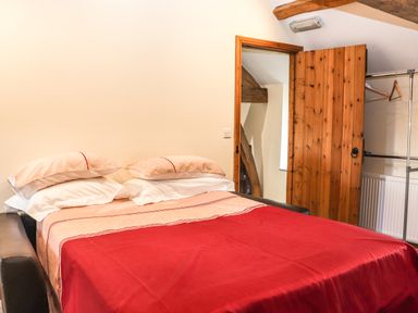 A bedroom with a bed with red and beige bedding and pillows next to a wooden door and a clothes rack at Maestyddyn Farm House in Clawddnewydd near Ruthin
