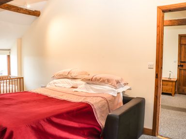 A bedroom with a bed covered with red and beige bedding and a wooden crib by the window at Maestyddyn Farm House Clawddnewydd near Ruthin