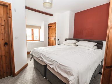 A bedroom with a double bed white bedding wooden doors and a window at Maestyddyn Farm House Clawddnewydd near Ruthin
