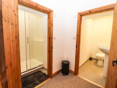 A hallway with two open wooden doorways leading to a shower room on the left and a toilet room on the right at Maestyddyn Farm House in Clawddnewydd near Ruthin