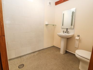 A bathroom with a toilet, sink with mirror, tiled wall, and wall-mounted glass shelf at Maestyddyn Farm House Clawddnewydd near Ruthin