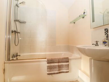 A bathroom with a bathtub shower combination a washbasin and hand soap at Maestyddyn Farm House in Clawddnewydd near Ruthin