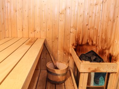 A wooden sauna with a bench a bucket with a ladle and a heater with stones at Maestyddyn Farm House Clawddnewydd near Ruthin