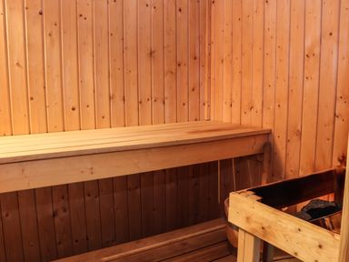 A wooden sauna interior with a bench and a heater containing sauna stones at Maestyddyn Farm House Clawddnewydd near Ruthin