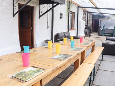 An outdoor dining area with wooden tables and benches set with colorful cups and placemats at Maestyddyn Farm House in Clawddnewydd near Ruthin