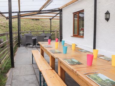 An outdoor covered dining area with wooden tables and benches with placemats and colorful cups at Maestyddyn Farm House in Clawddnewydd near Ruthin